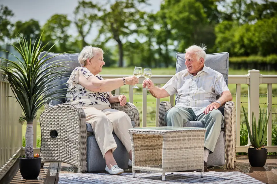 Elderly couple enjoying drinks on their caravan decking at Eryl Hall Holiday Park