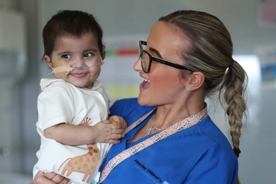 Aldery Hey childrens specialist holding young child: Charity of the year for Lyons Holiday Parks